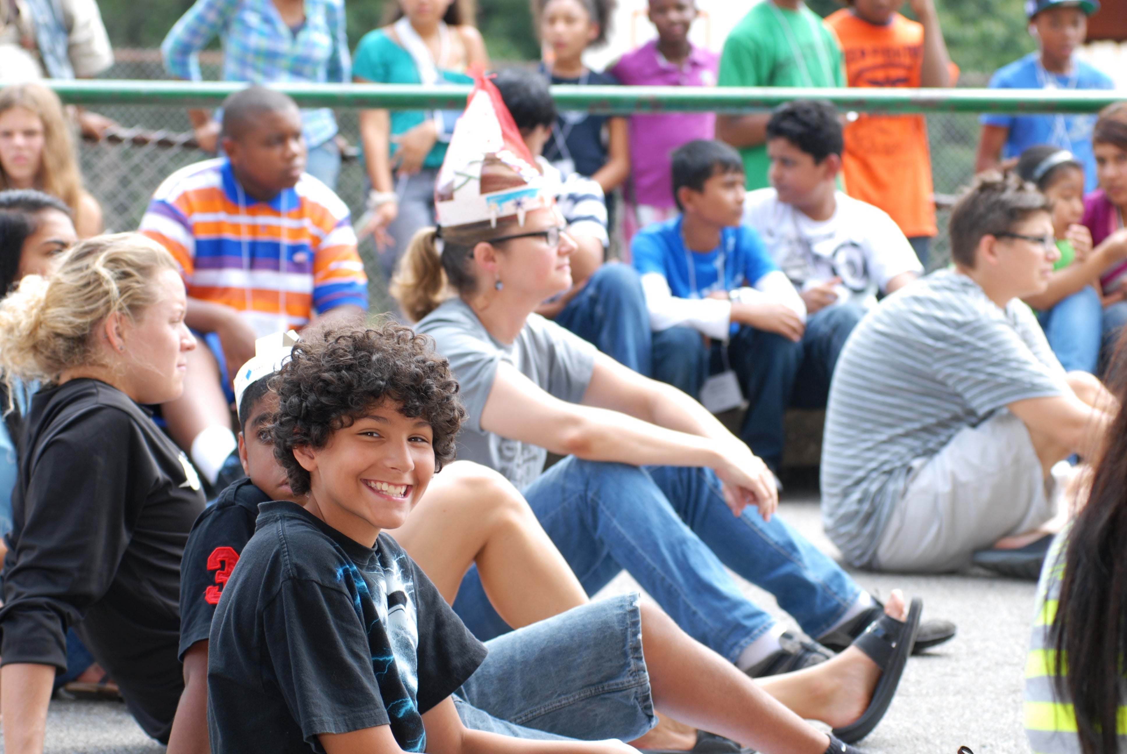 A boy smiles at the camera as children watch a performance.