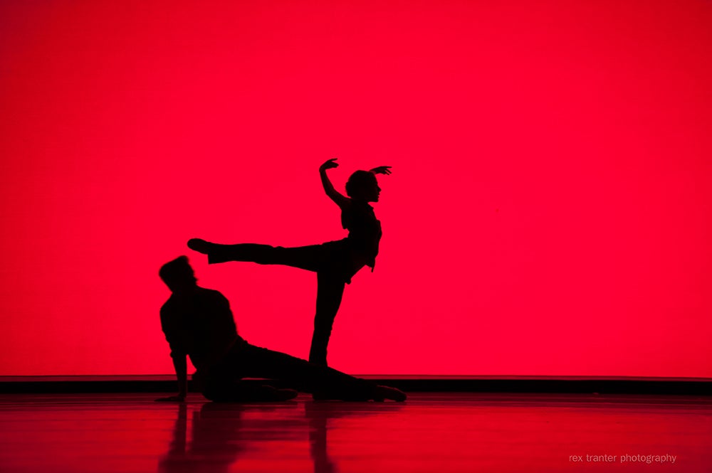 Two dancers silhouetted against a red backdrop on stage.