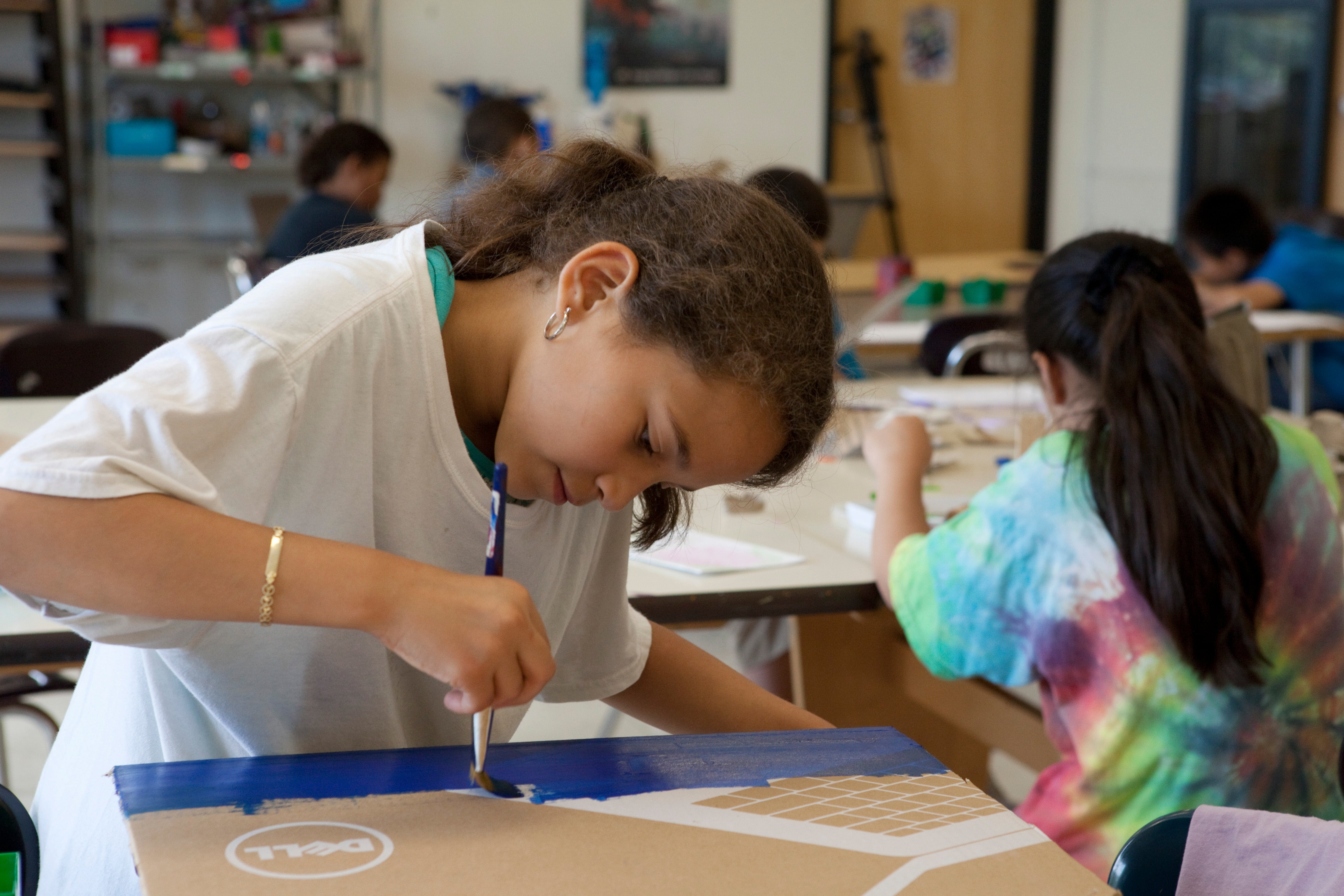 A girl uses a paintbrush with blue paint to work on her artwork.