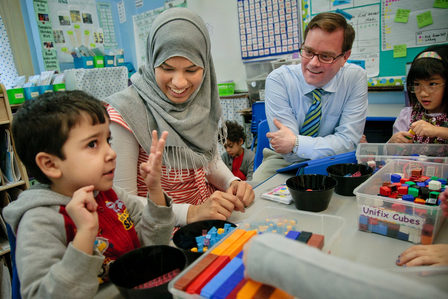A principal sits with a teacher and students at a table full of learning blocks.