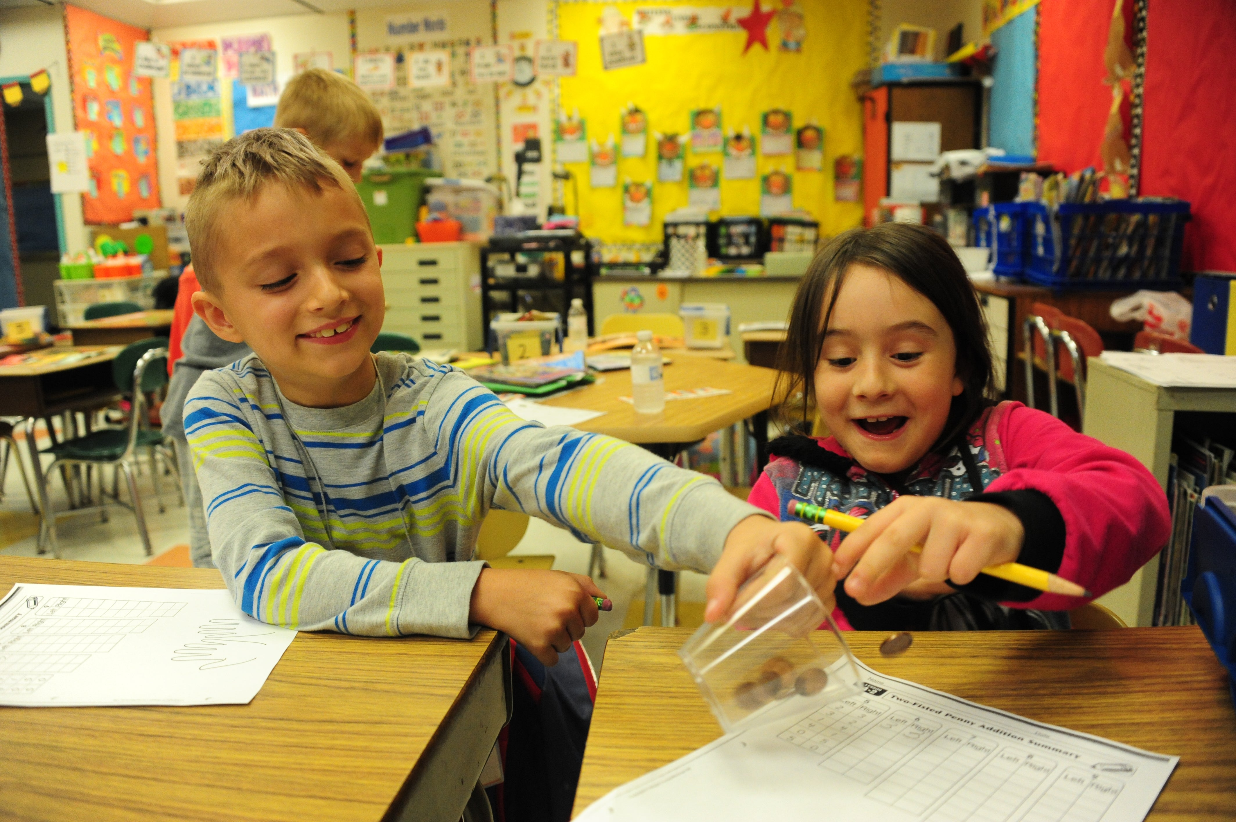 Two students sit at their desks and play with a plastic cup during their program.