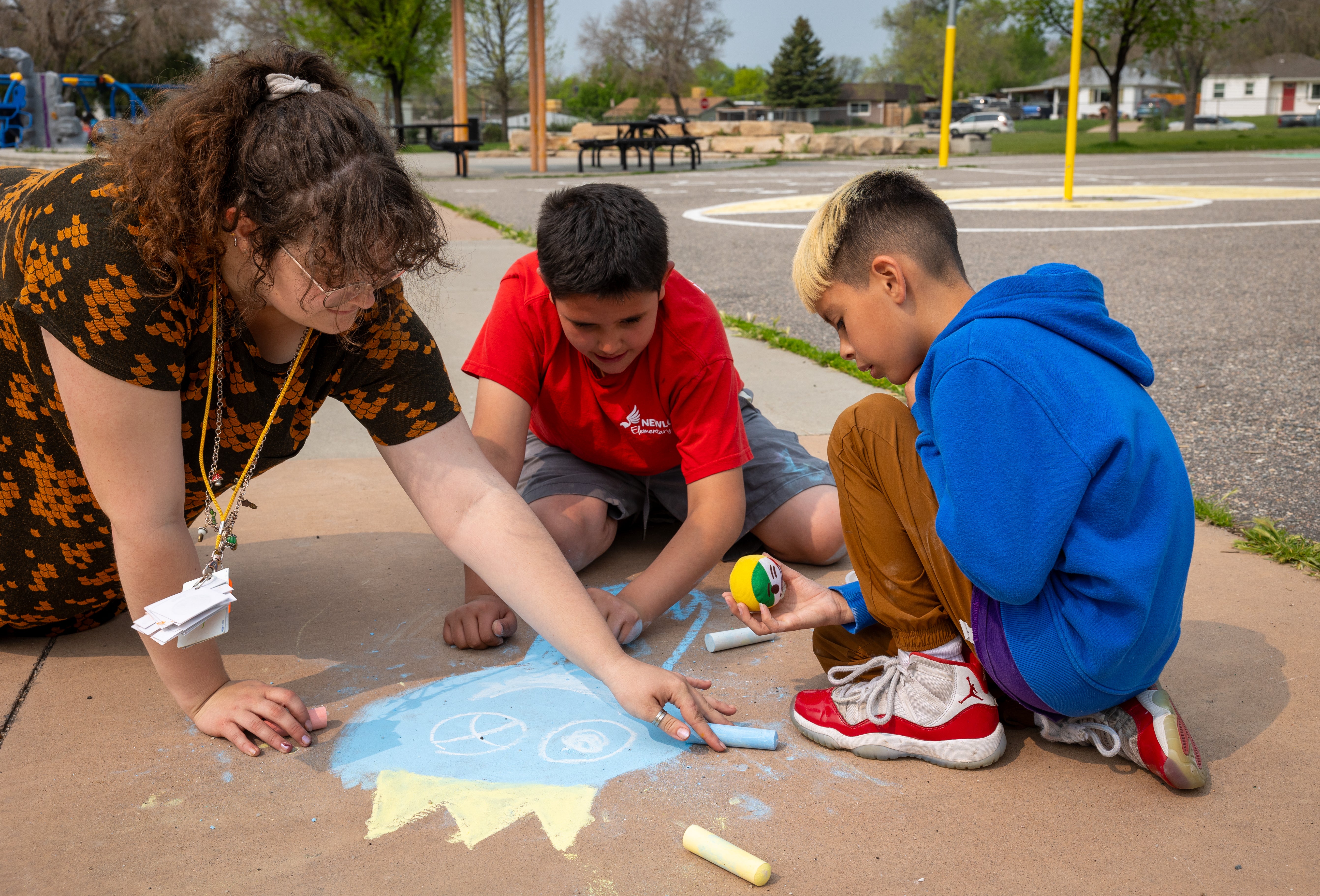 Students colour in a drawing on the sidewalk with chalk.