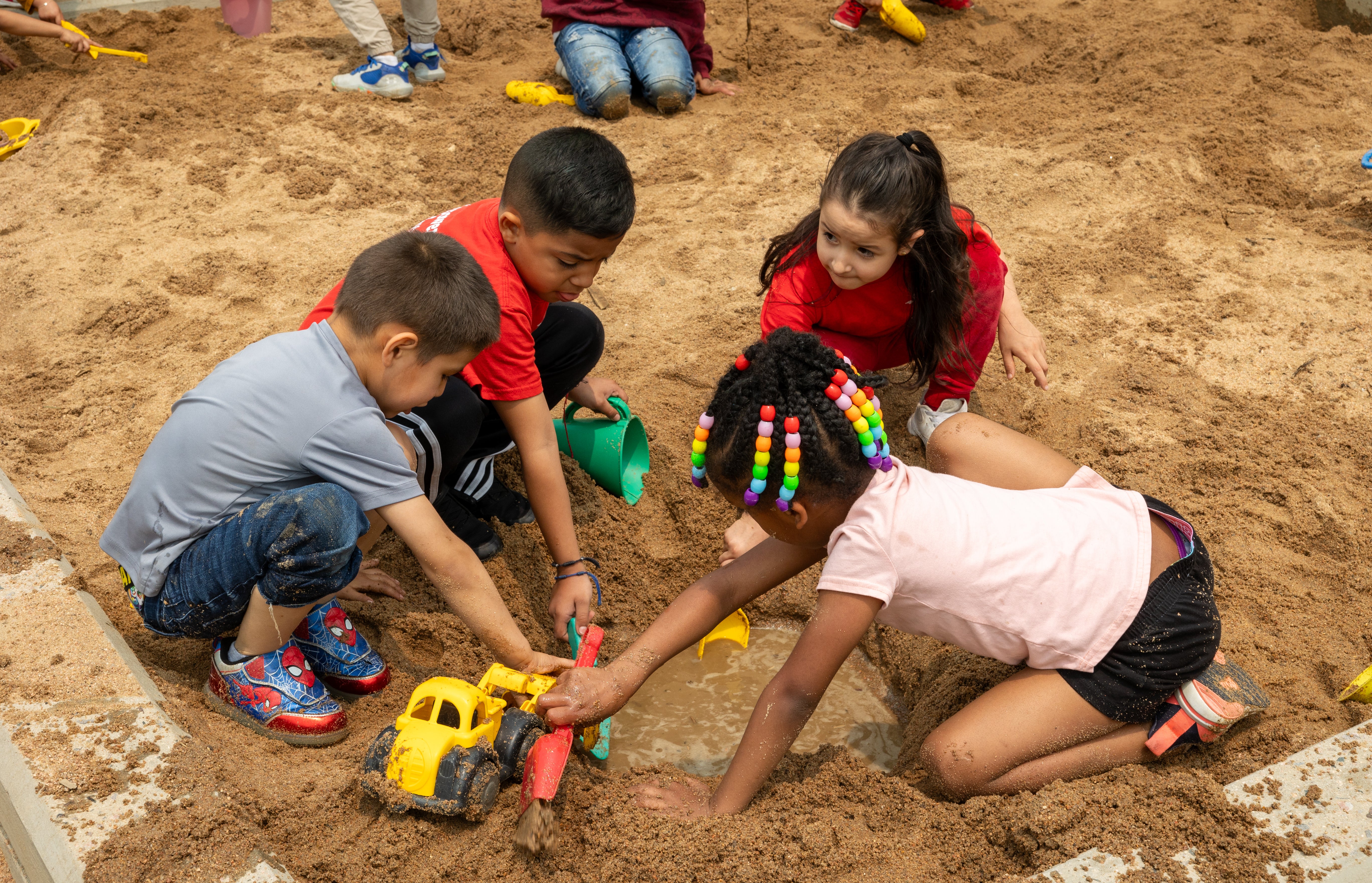 Children in a sand pit play with toys.