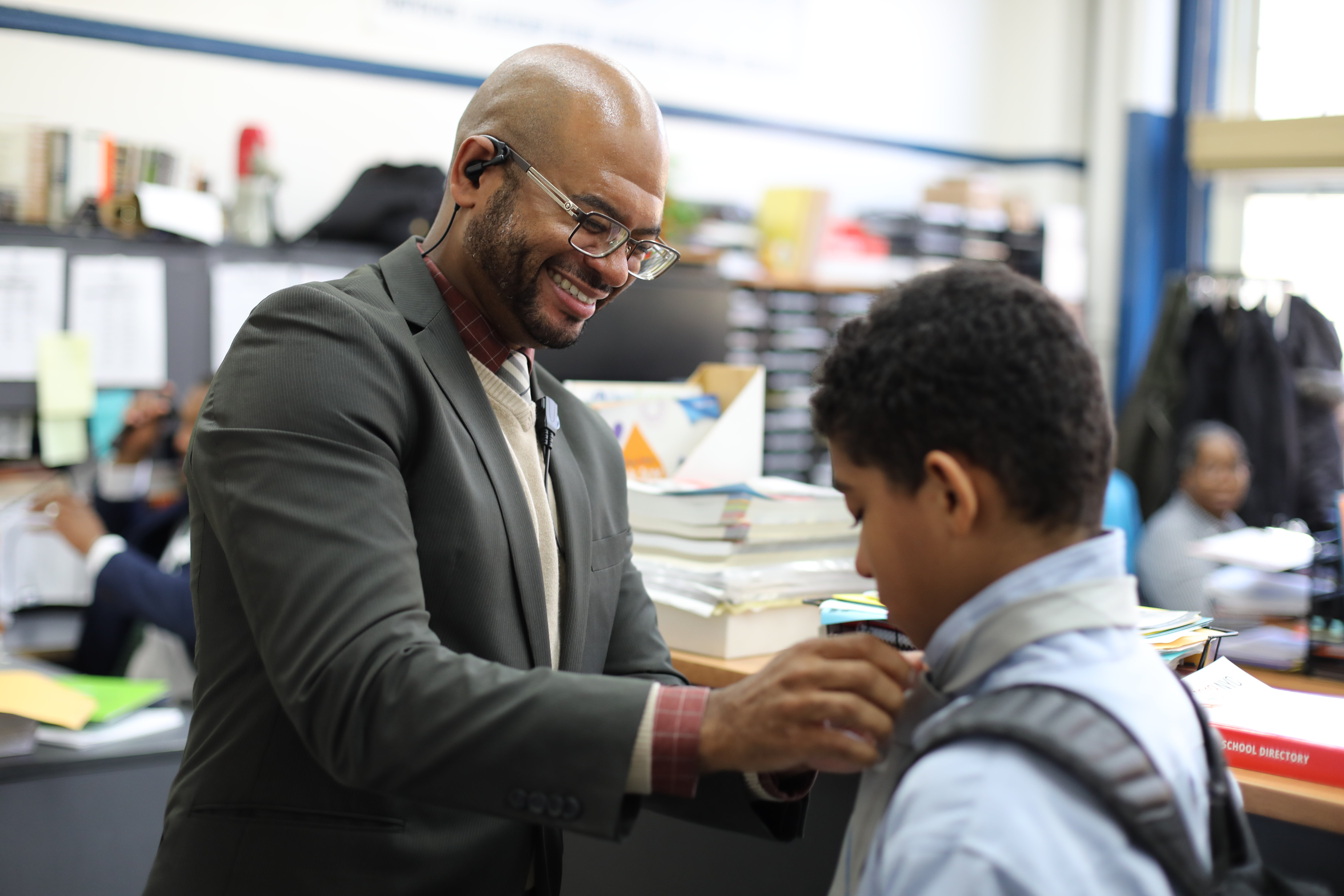 A school principal adjusts a student's collar for him.
