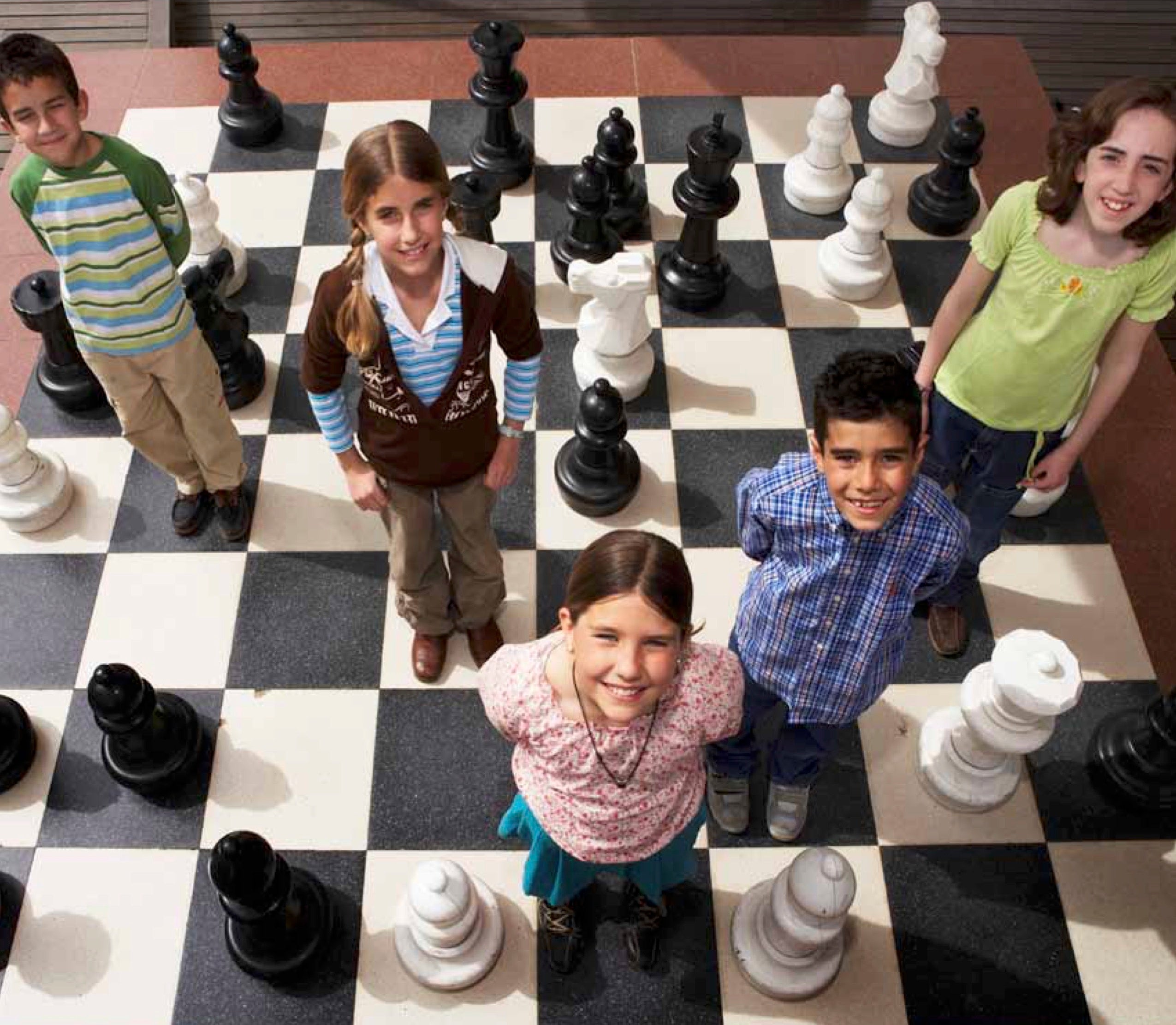 Children stand amongst life-sized chess pieces and look up to smile towards the camera.