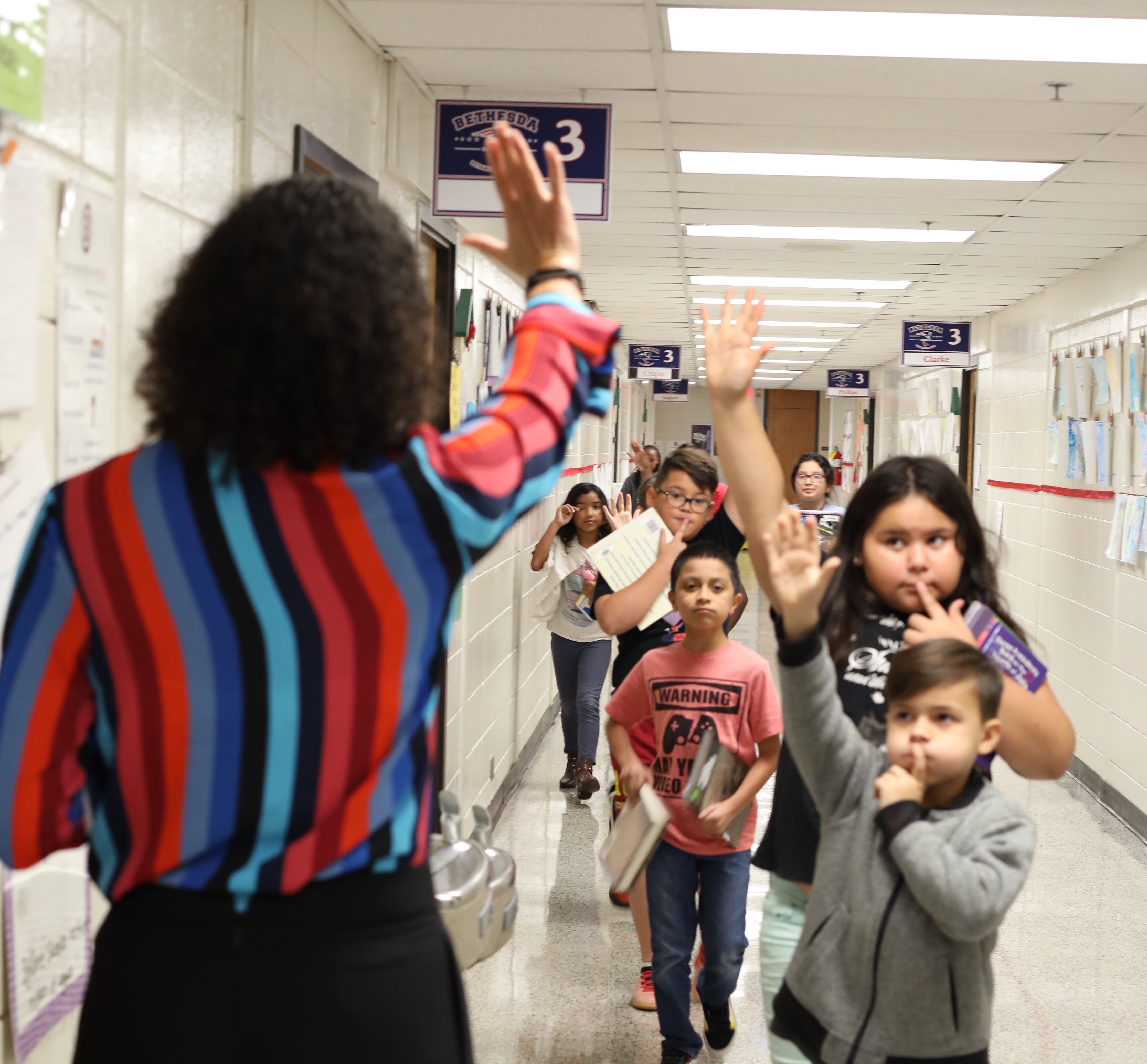 A school principal offers high-fives to students in the hallway.