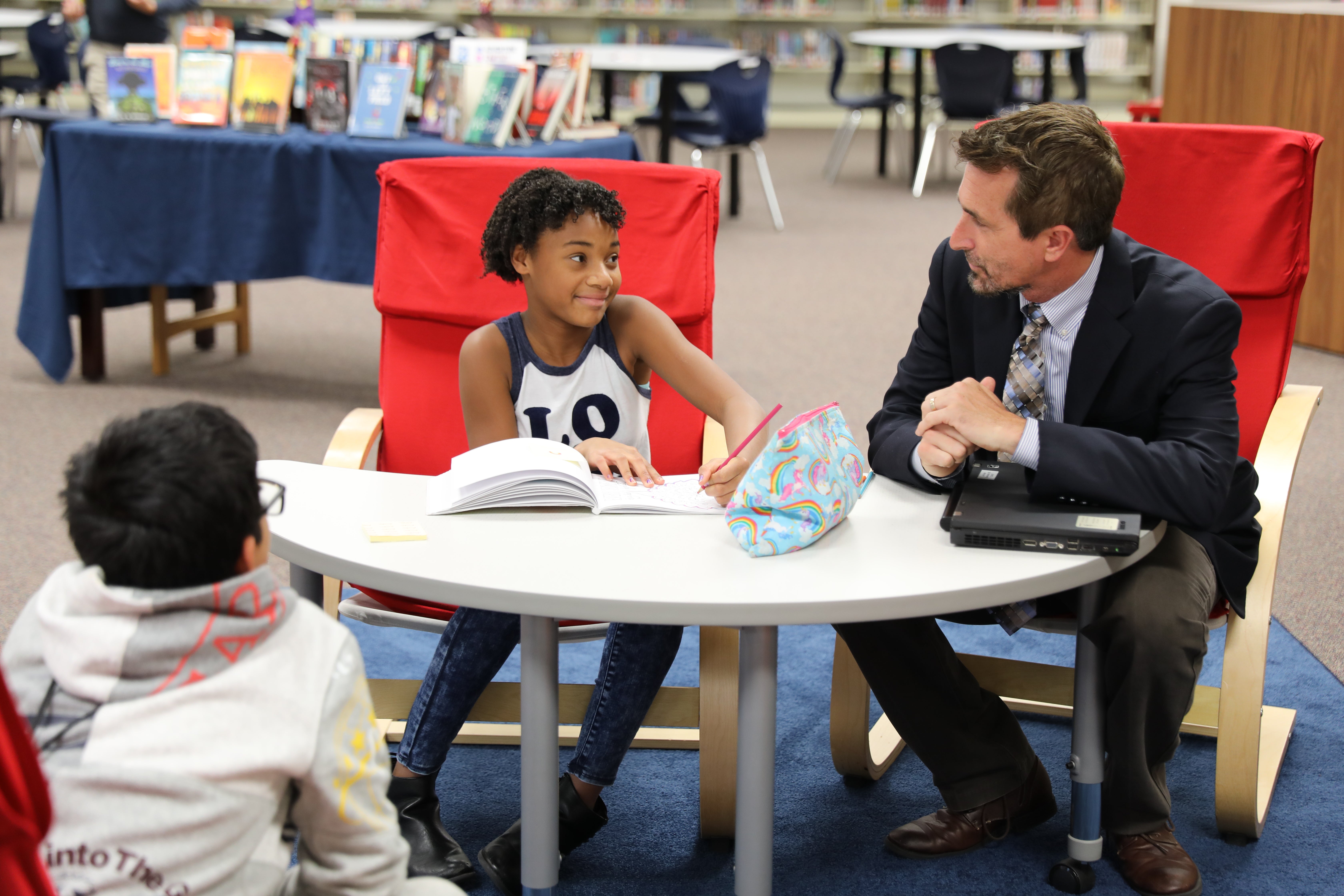 A school principal chats with two students in the library.