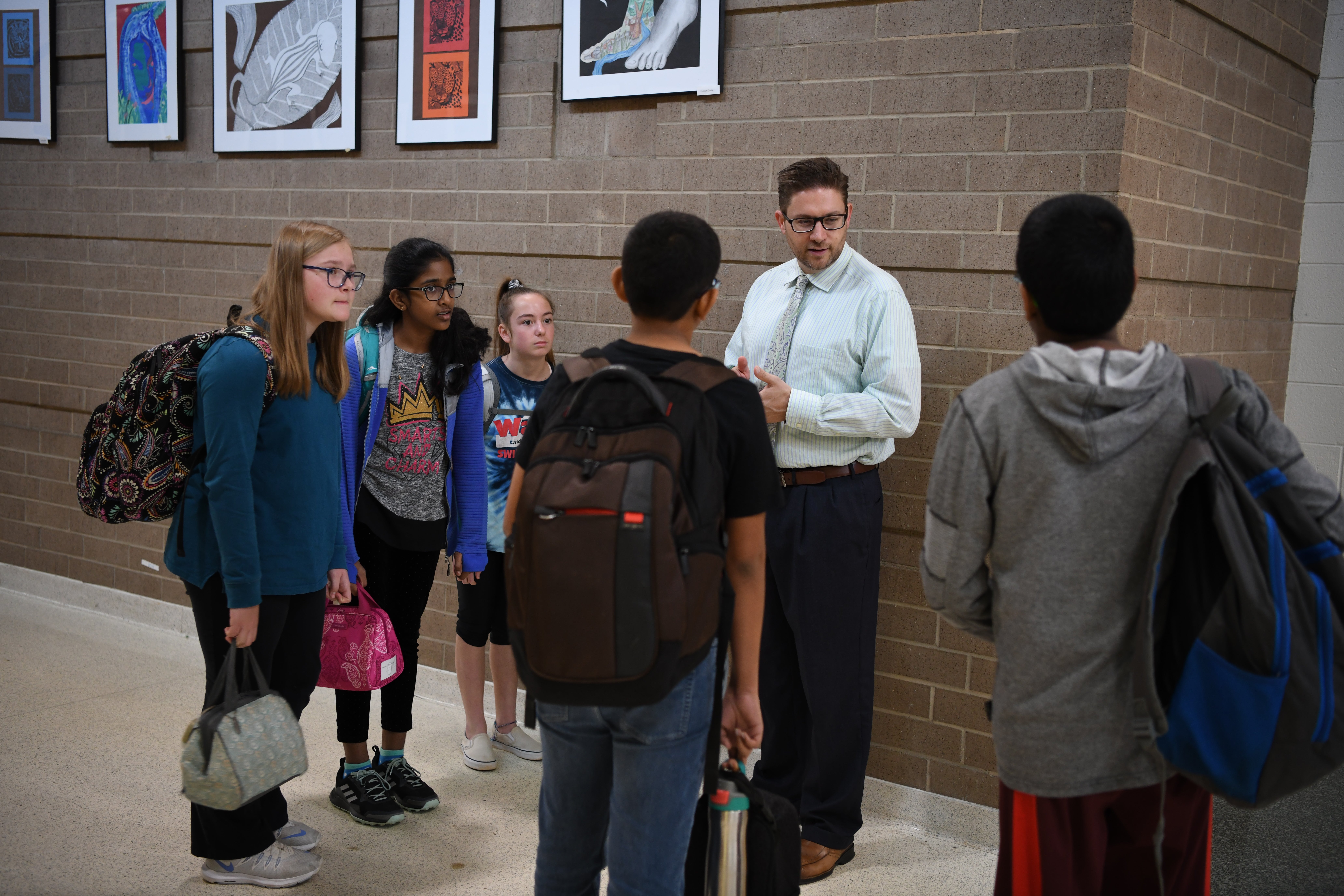 A school principal chats with students in the hallway between classes.
