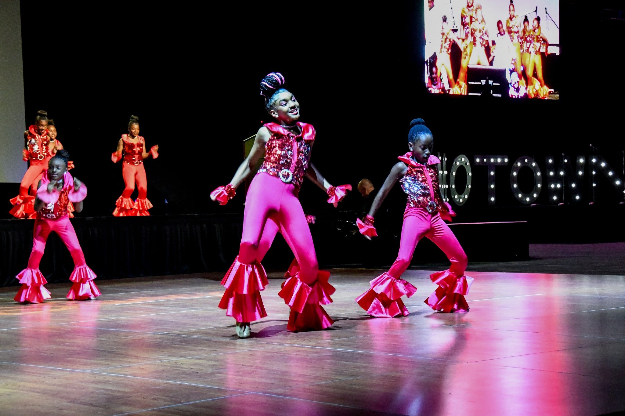 Youth in fuchsia outfits dance to Motown music on stage.