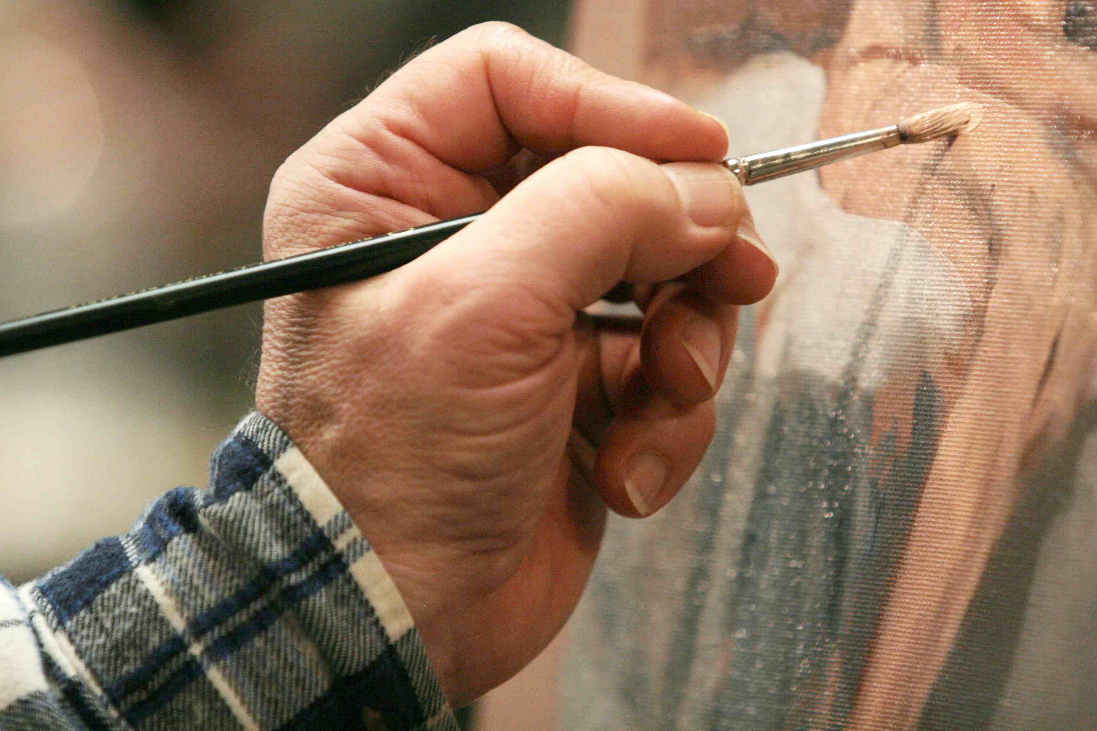 A close up shot of a hand holding a paintbrush to a painting.
