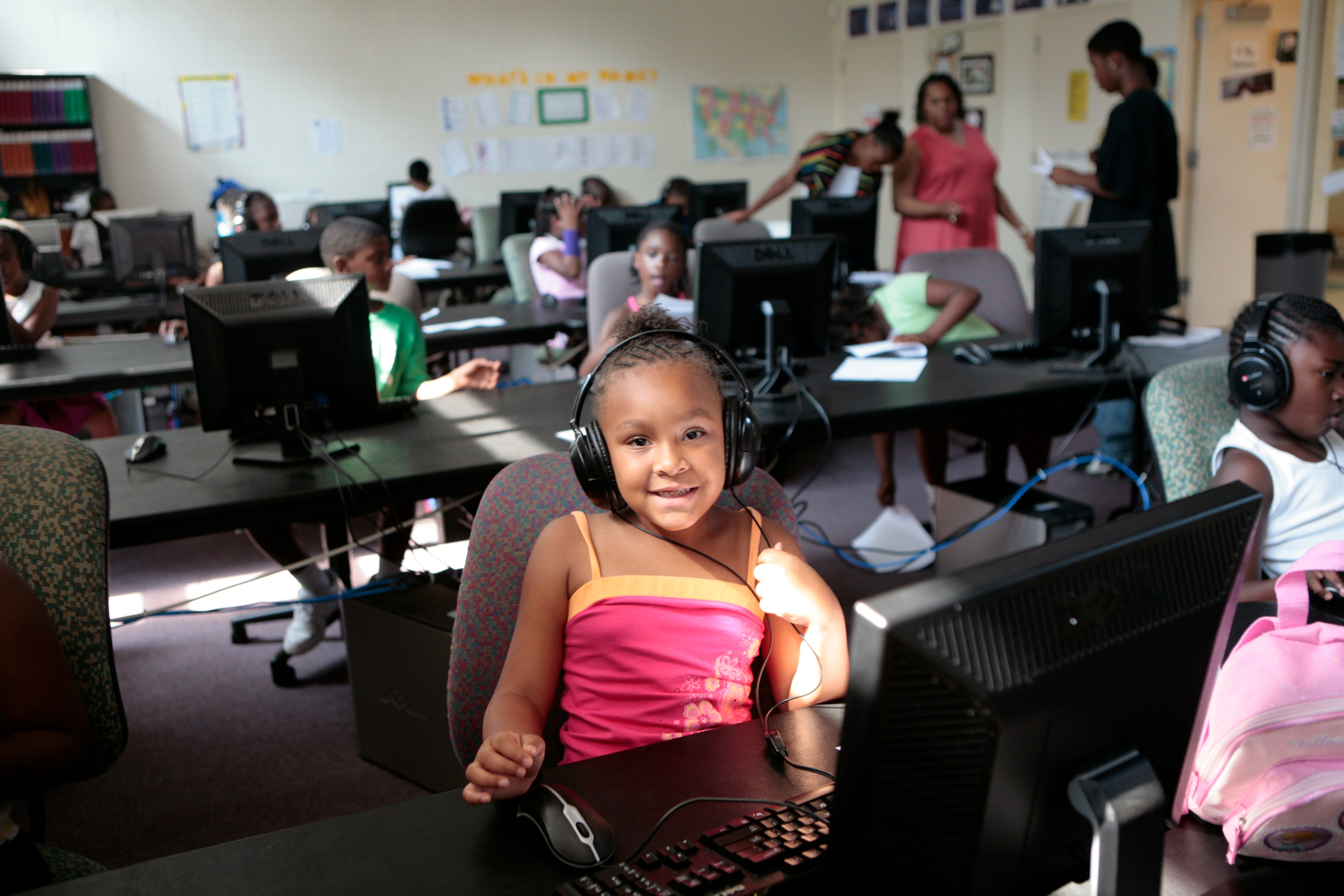 A girl wearing headphones in front of the computer smiles at the camera.