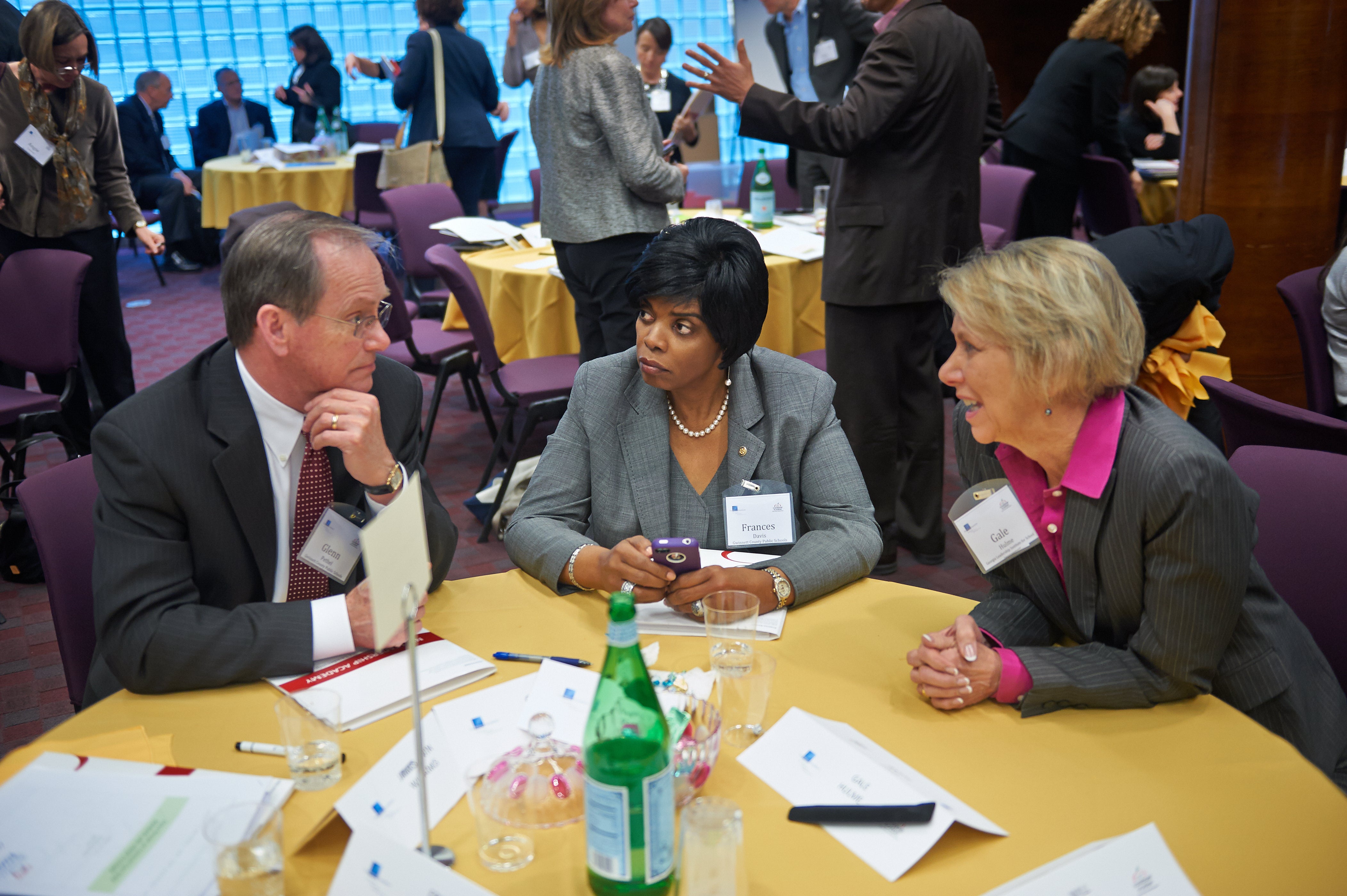 Three education leaders sit at a table in discussion during a conference.