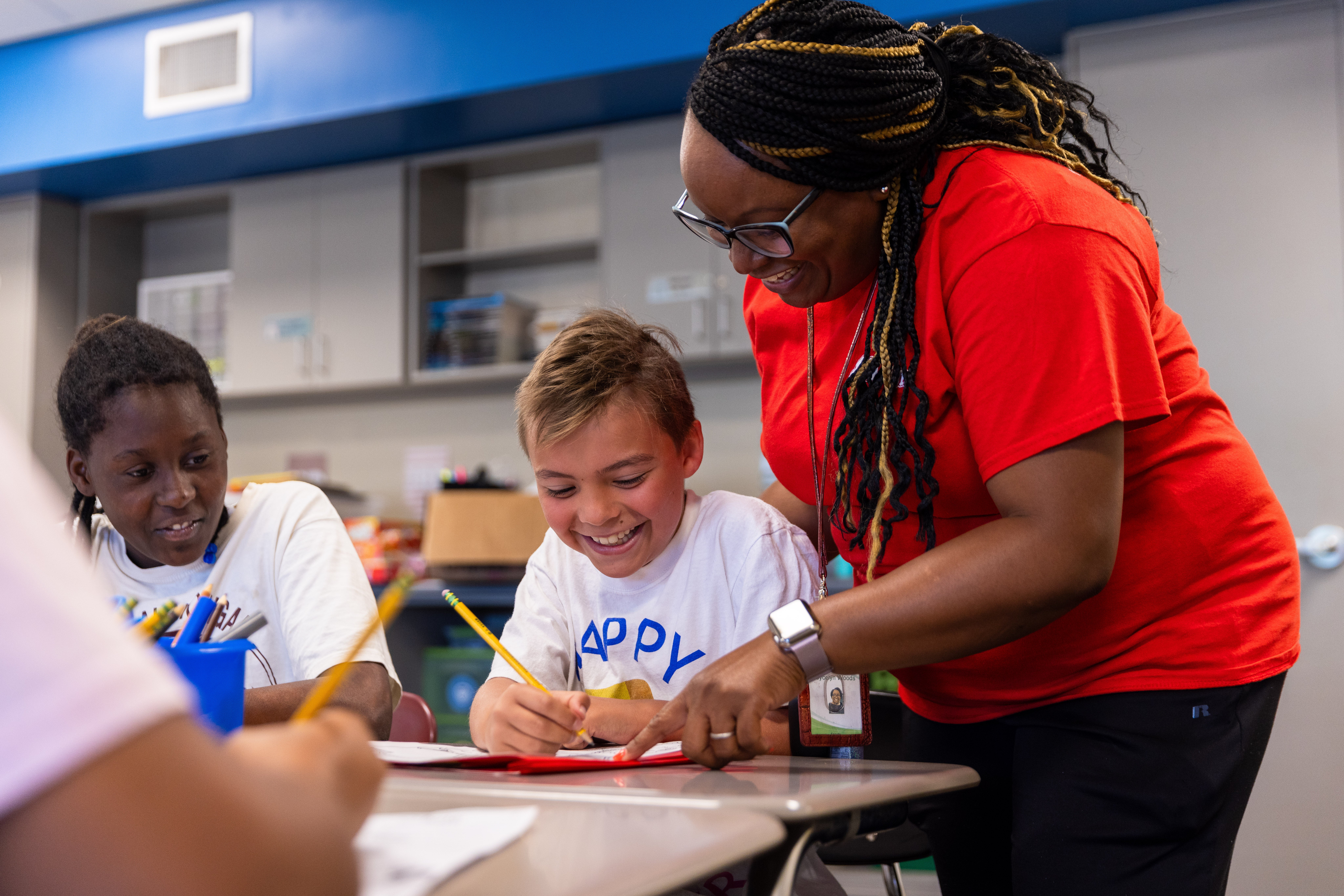 A teacher guides two students in their summer program work.
