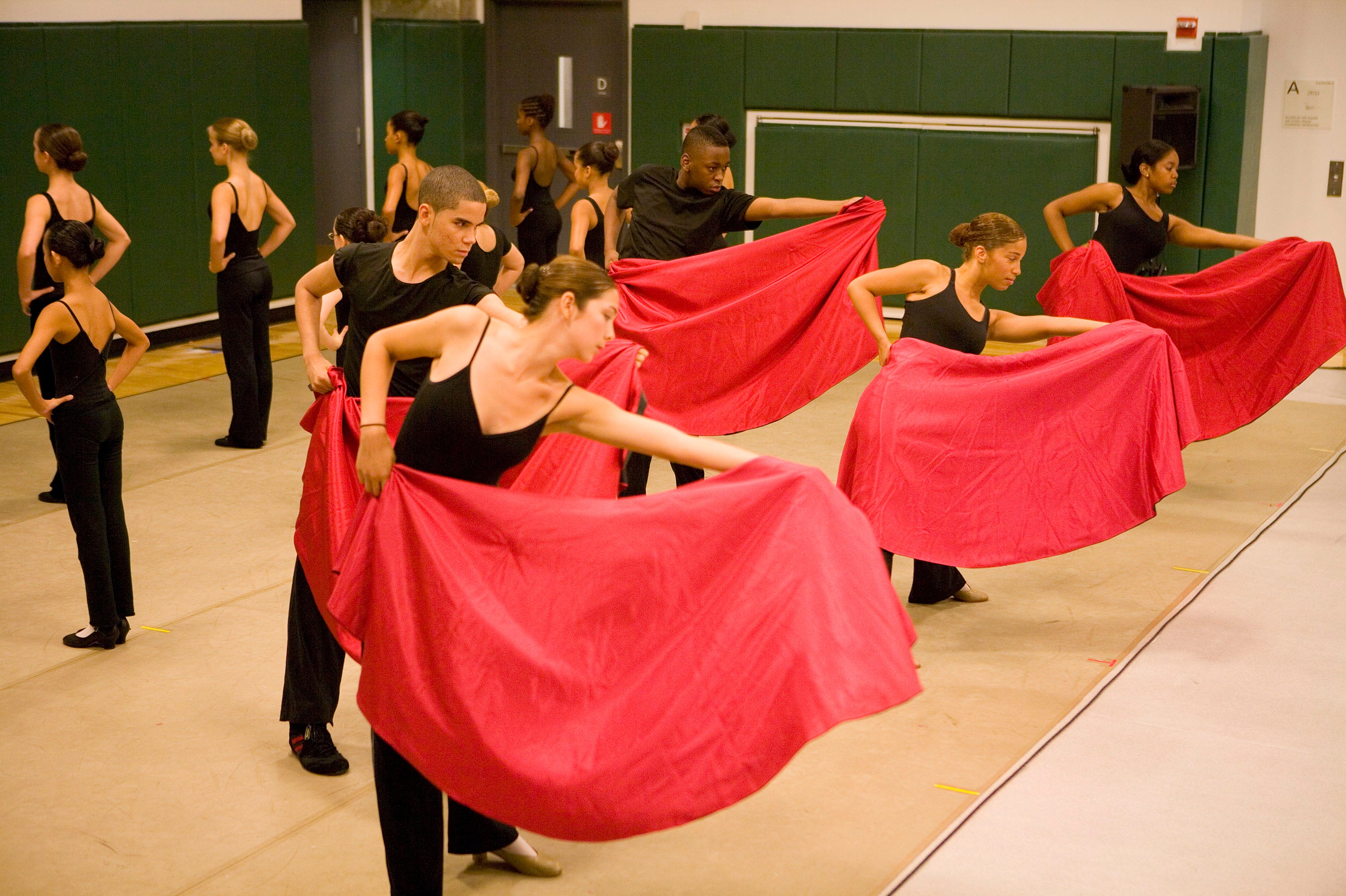 Dancers in black hold out red sheets during their performance practice.