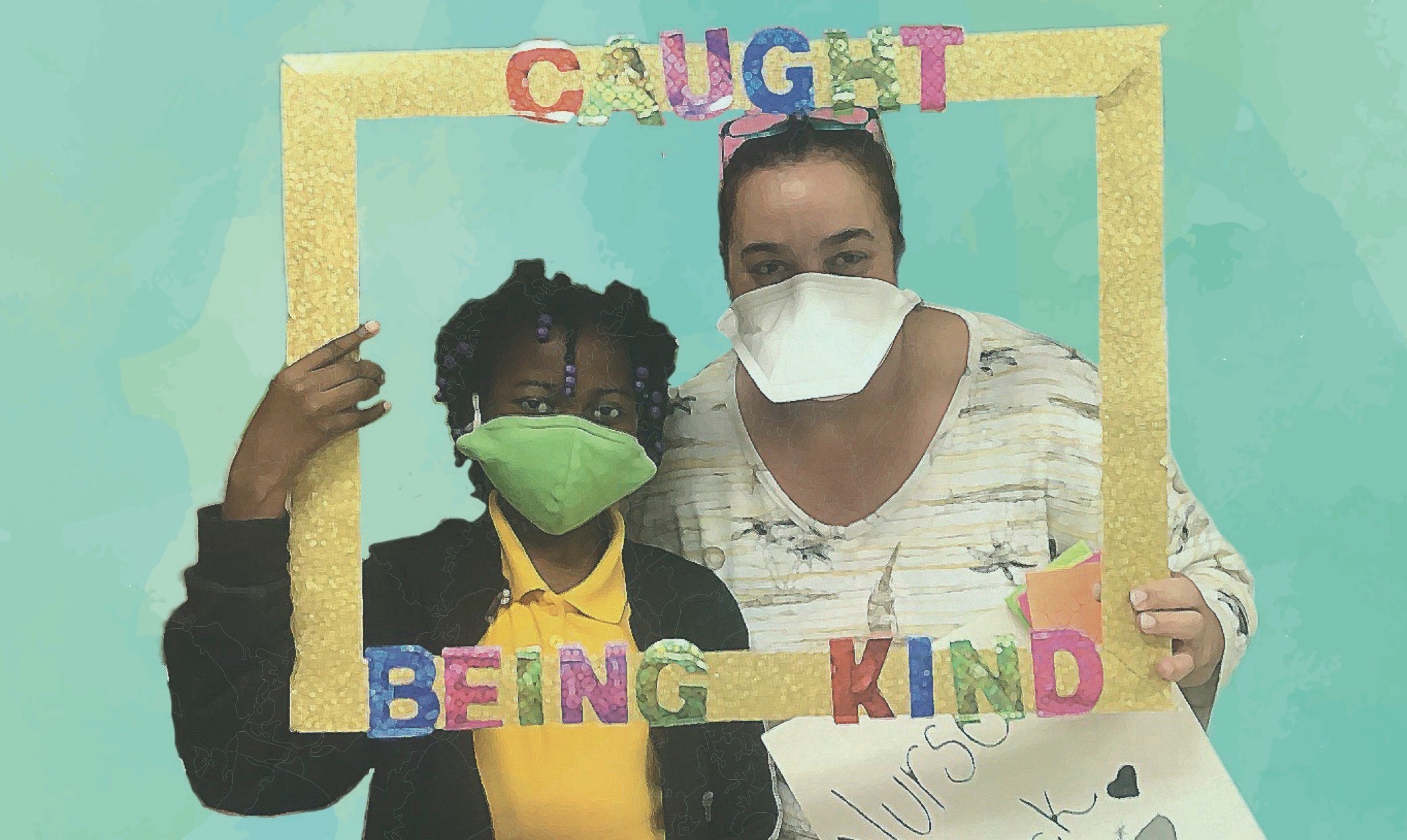 A teacher and student wearing masks hold up a handmade frame that reads "Caught Being Kind"