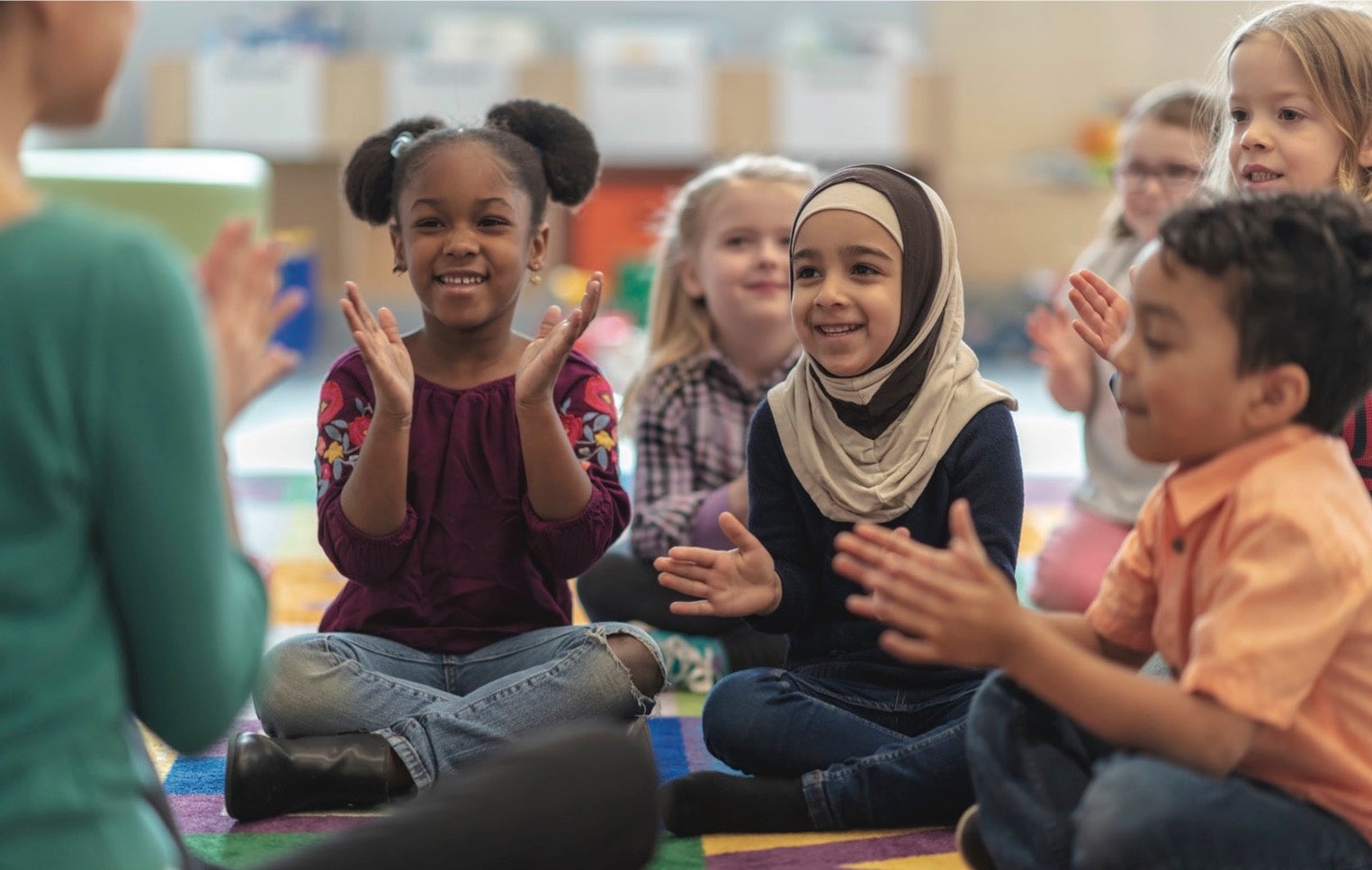 Children sit on the floor clapping with their program leader.