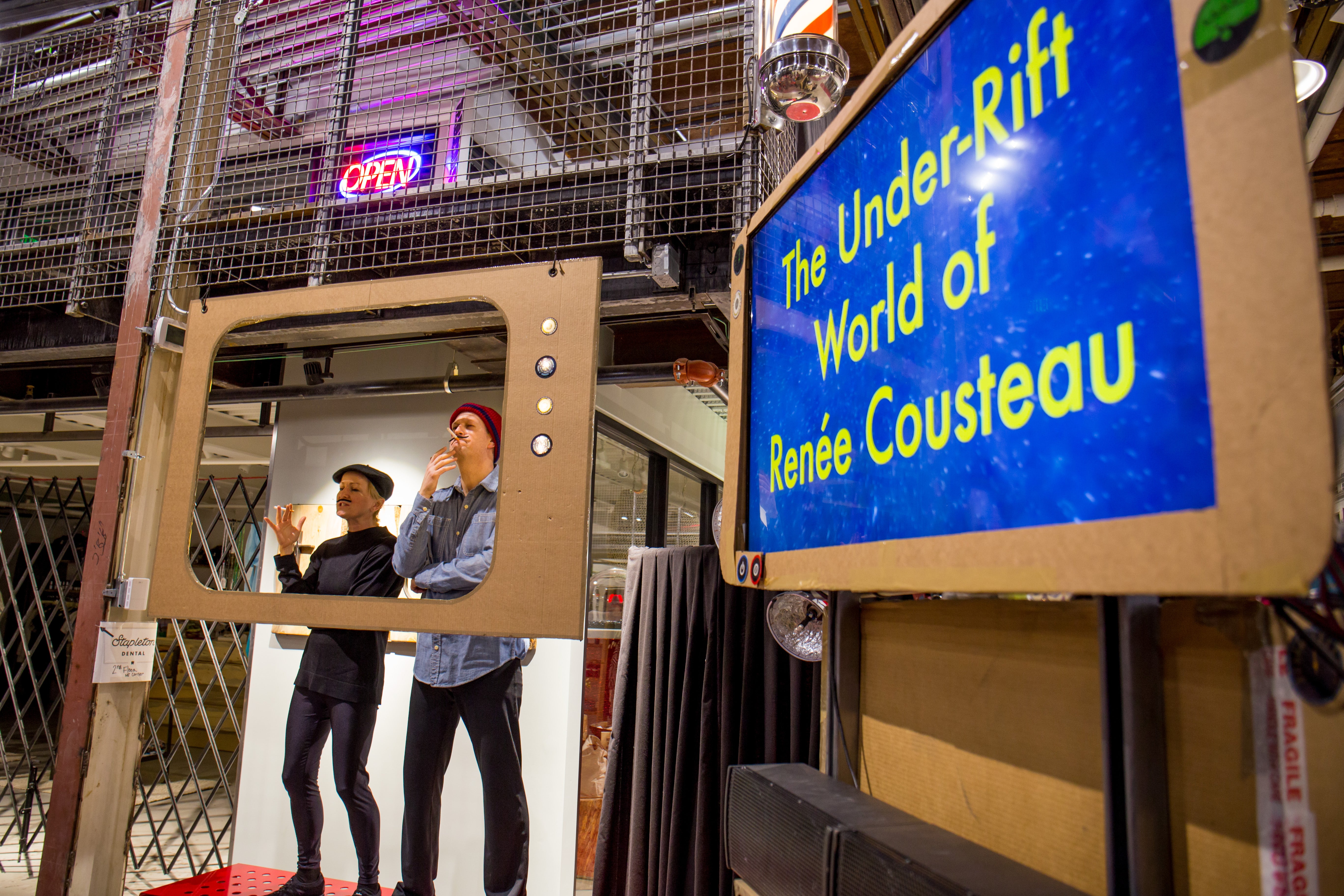 Two men stand behind a cardboard frame in front of a sign reading "The Under-Rift World of Renee Cousteau".