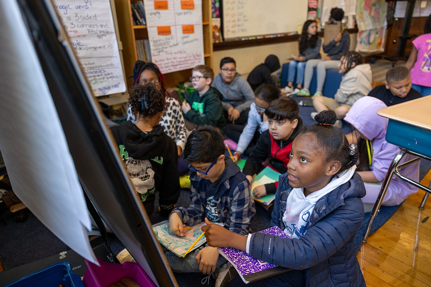 Black, white and other children in a classroom looking at a board, in Boston