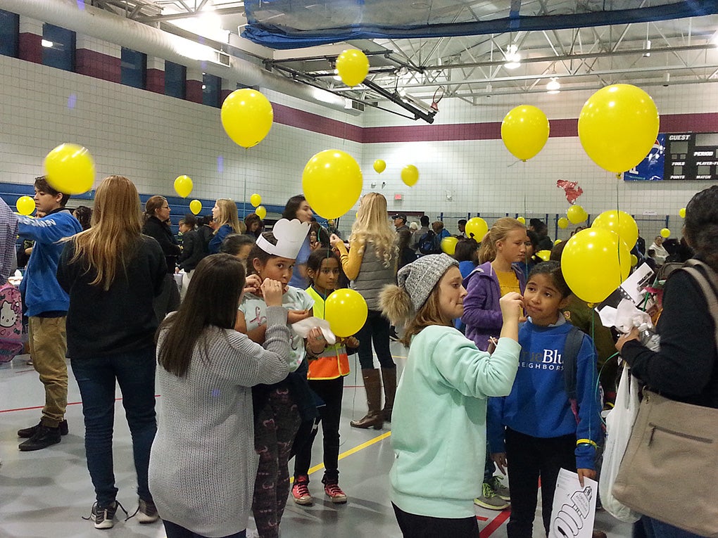Teen students stand about a gymnasium with yellow balloons.