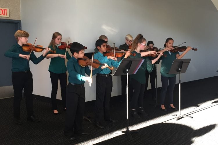 A group of students in uniform play their violins.