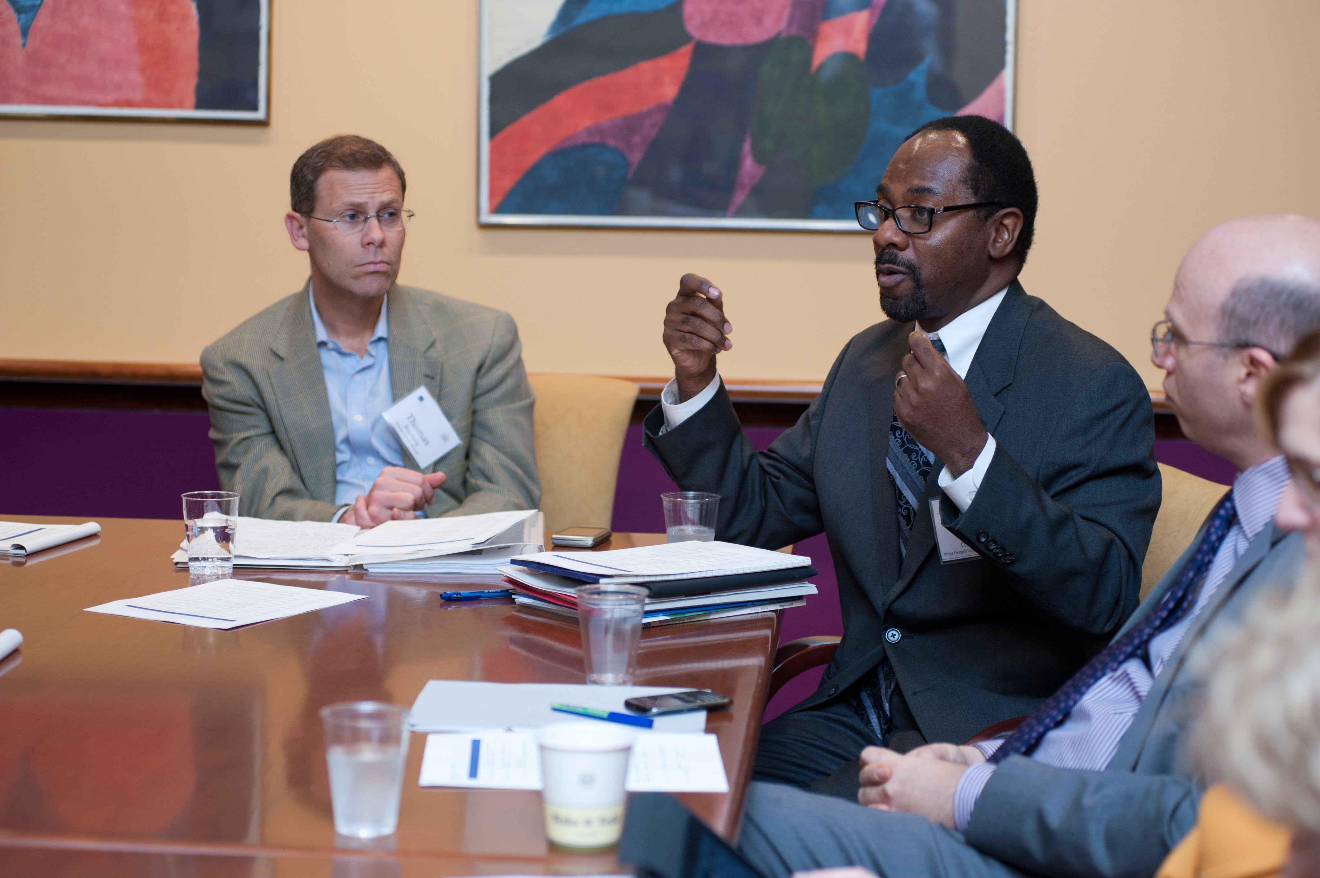 2 white men with 1 black man with glasses sitting at a conference table. NYCLA