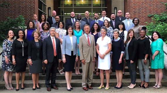 A group of education leaders pose for the camera in front of a building.