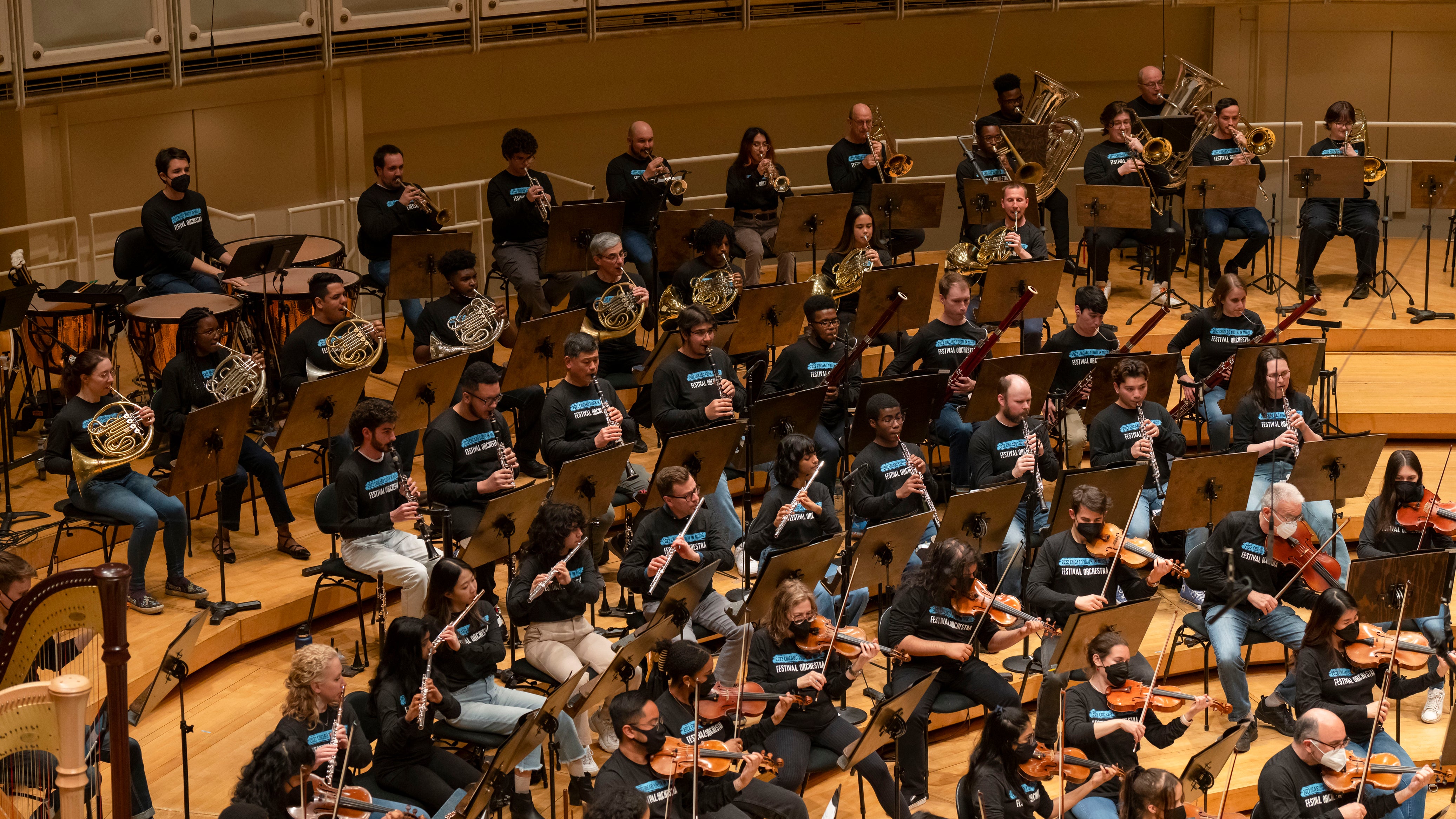 Members of the Chicago Symphany Orchestra rehearse in concert hall, strings in front, wind instruments, horns and percussion in back