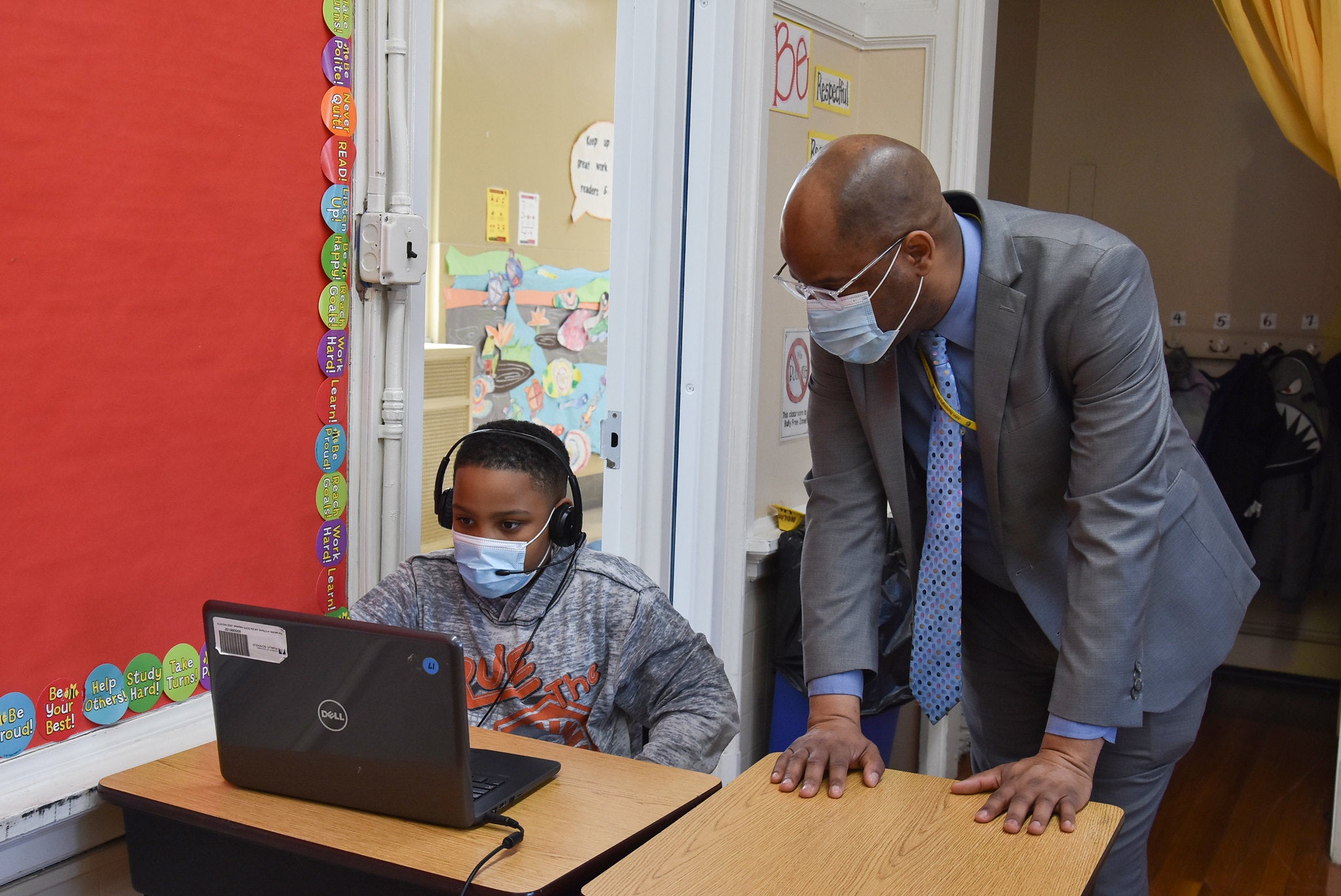 A teacher and student in masks look at a laptop screen.