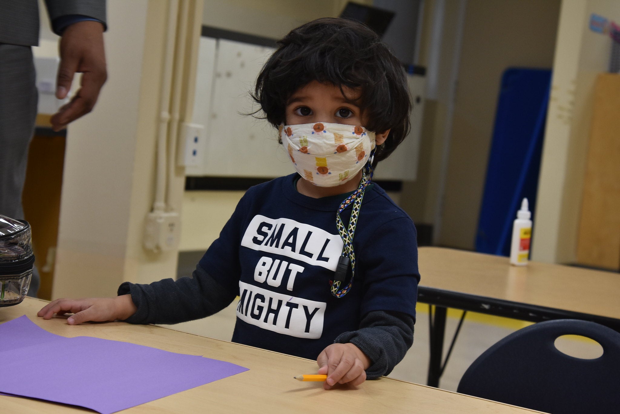 A young student wearing a mask and a shirt that reads "Small but mighty".