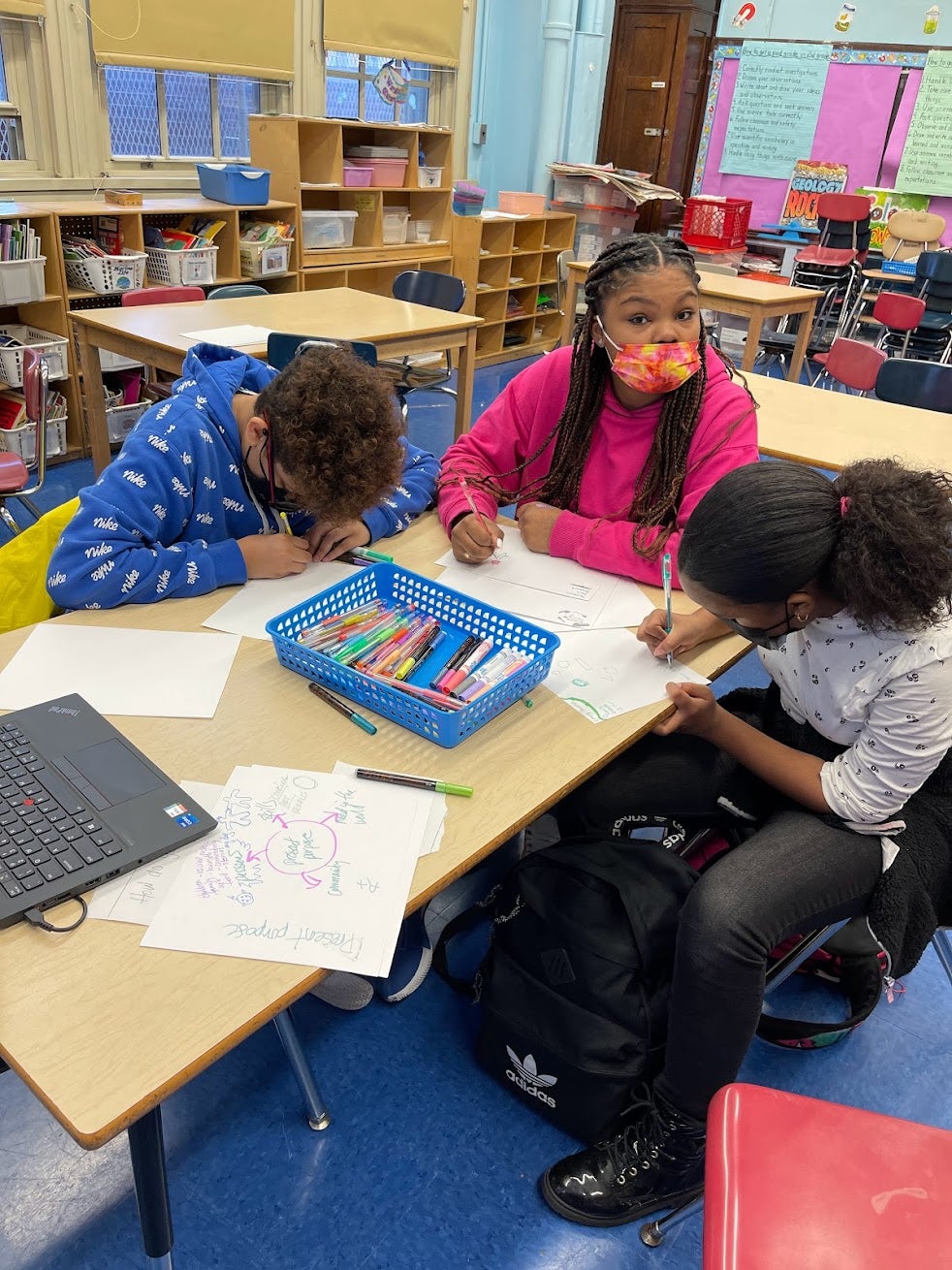 Students wearing masks work on their artwork at a table in a classroom.