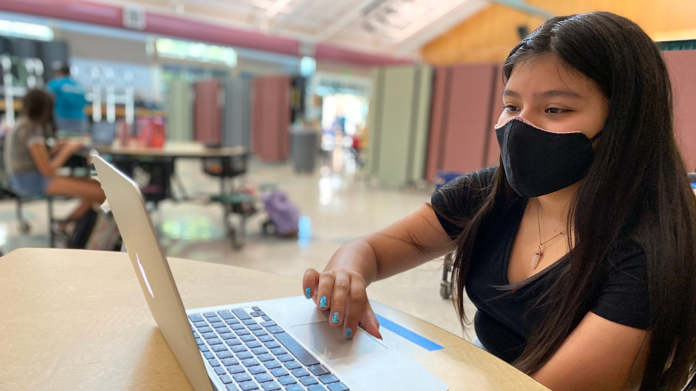 A student wearing a mask works on her laptop.