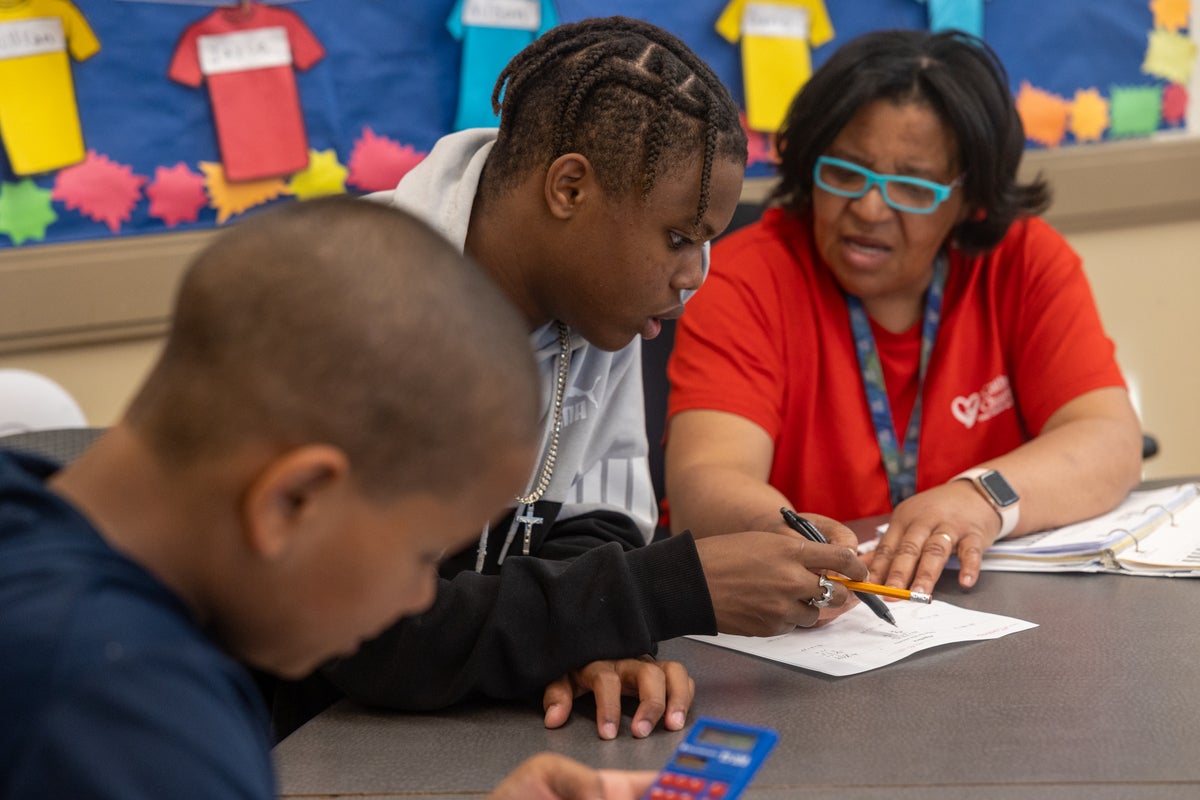 Black female teacher in red shirt helping two black teenage students with school work with pen and paper sitting at desk