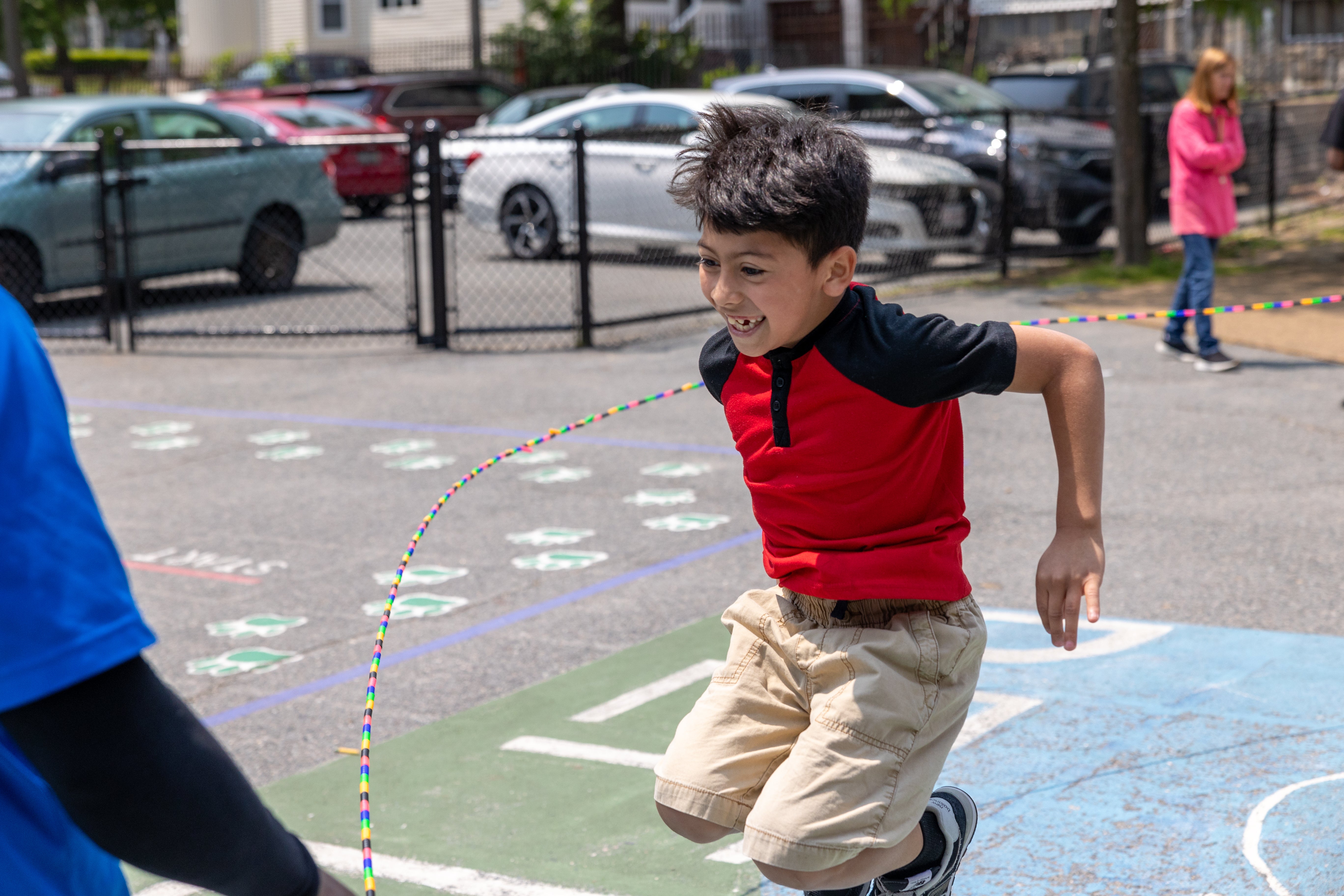 Boy wearing red and black short-sleeve shirt and khaki pants plays jump rope on a playground.