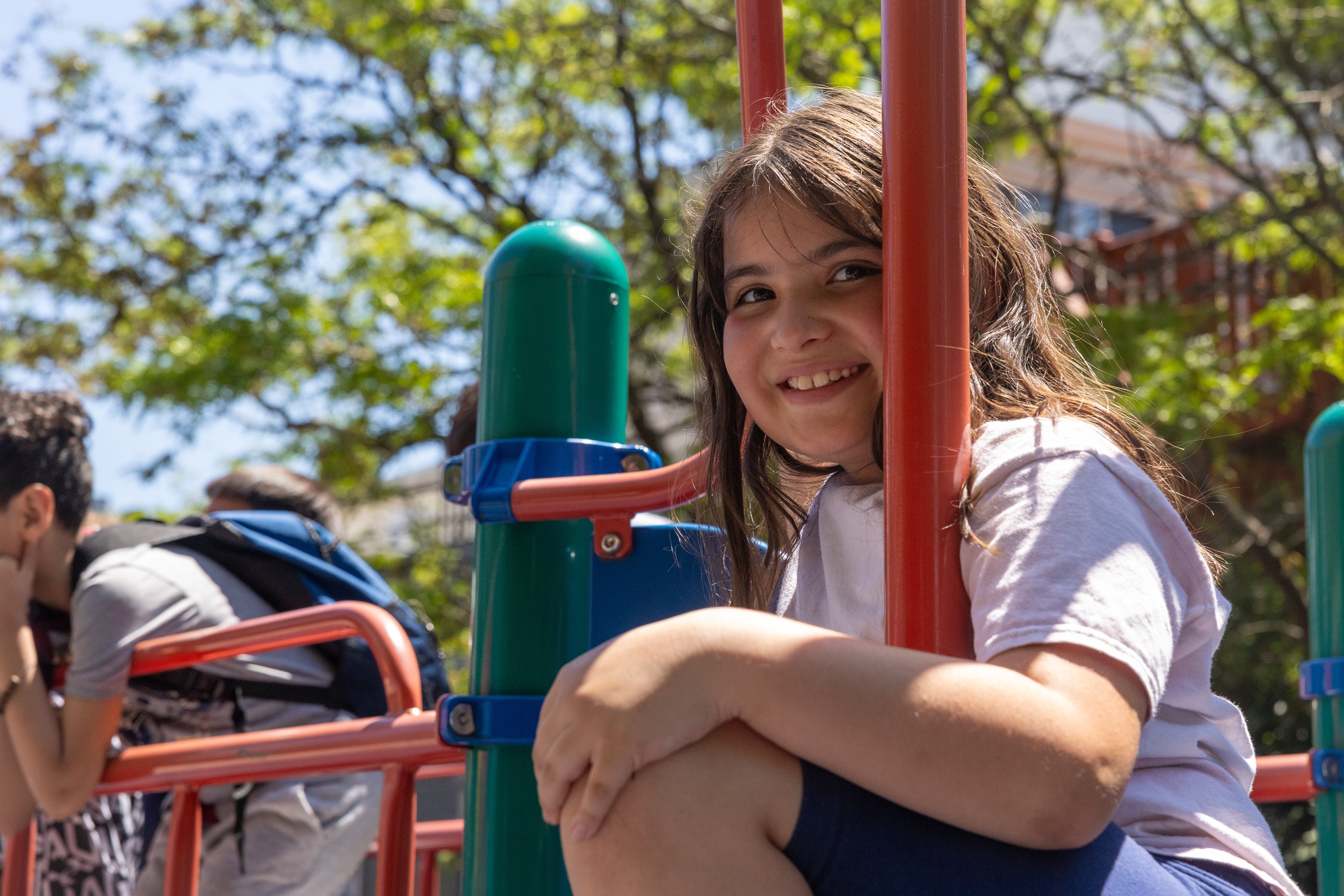 young girl smiles at the camera as she sits on a playground jungle gym